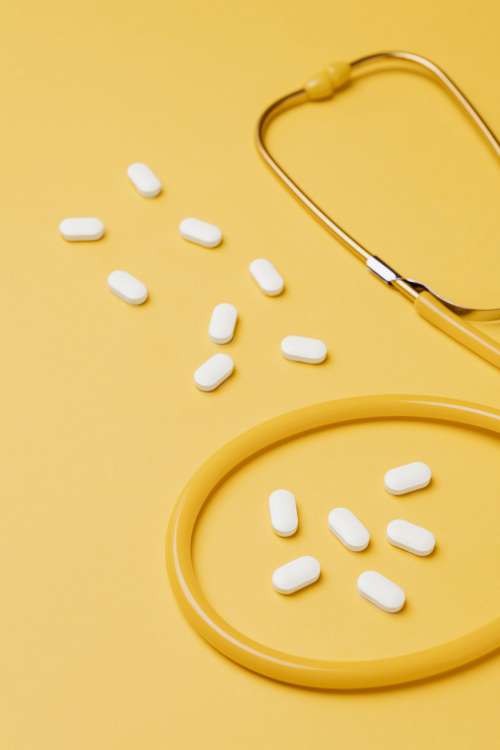 Yellow stethoscope and pills on yellow background