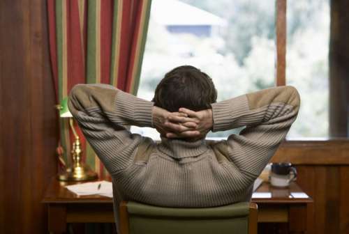 Man looking out of window, hands behind head, rear view