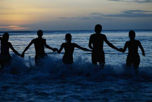 Group of people holding hands in sea, silhouette