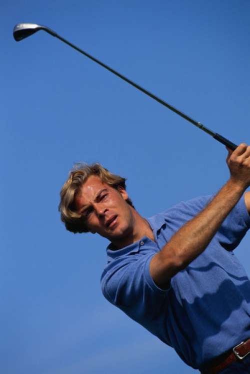 Man swinging golf club, low angle view