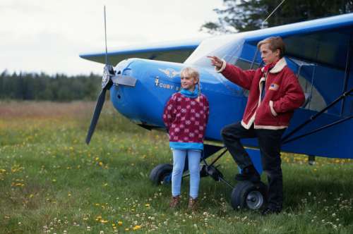 Girl and boy leaning against aircraft