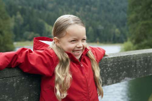 Girl (5-7 years) leaning against footbridge over lake, smiling, close-up