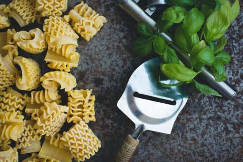 Pasta with a cheese grater and basil on a rusty metallic background