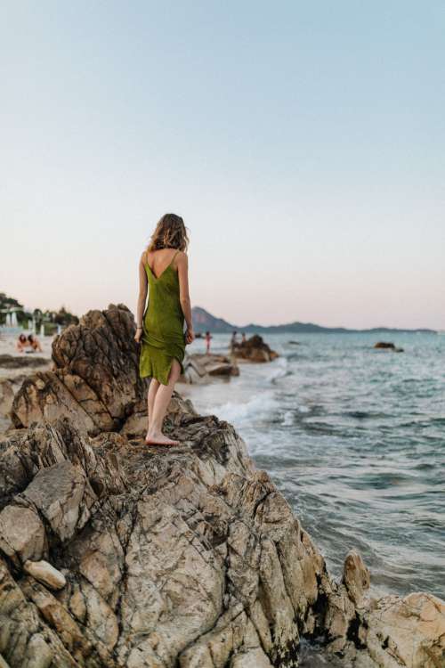 A woman in a green dress on a rock by the sea