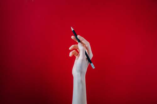 Hand Holding Black Pencil On Red Background Photo