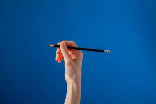 Hand Holding Black Pencil On Blue Background Photo