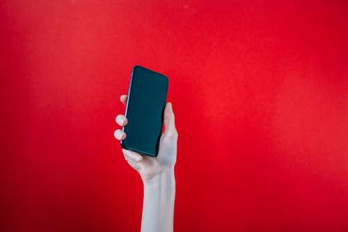 Hand Holds Up Black Mobile Phone On Red Background Photo