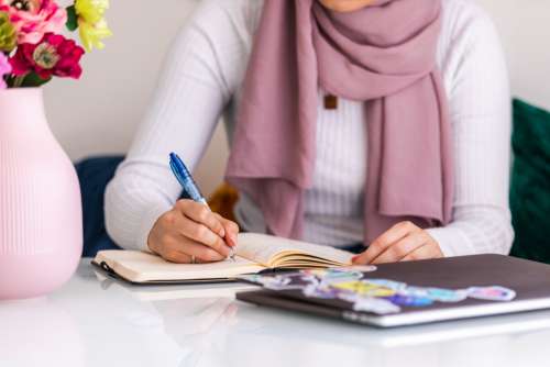 Woman Sits At Table Making Notes In Journal Photo