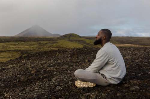 Young Man in Grey Sweatshirt Sitting Alone Near Mountains