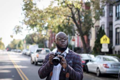 Young photographer in glasses holding DSLR camera on the street