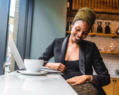 Smiling Young Woman in black blazer with laptop in Coffee Shop