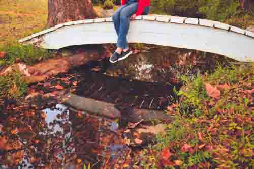 Girl Sitting On Bridge With Stream And Fall Leaves