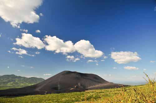 Black Volcano And Mountain In Perfect Blue Sky With Fluffy Clouds