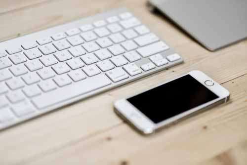 iPhone On Wooden Desk With Keyboard And Track Pad