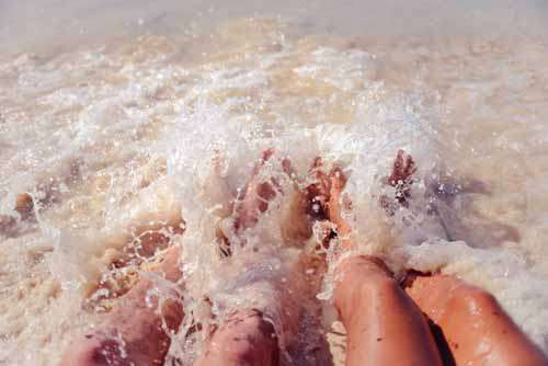 Man And Woman Feet Playing In Waves On A Beach