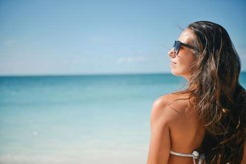 Girl In Bikini Wearing Sunglasses On A Beach Looking At The Sun