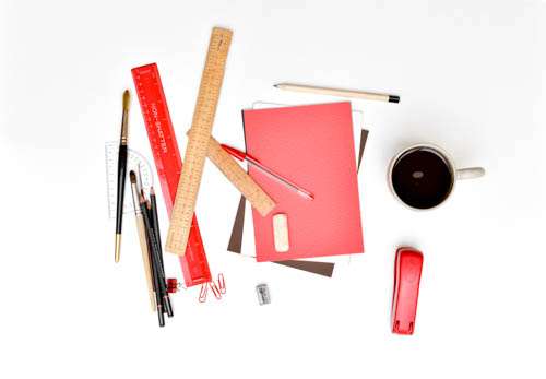 Messy Assorted Stationary On White Desk And Coffee