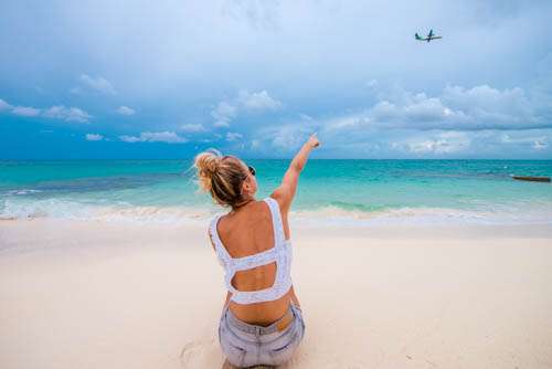 Girl Sitting On Beach Pointing At Airplane