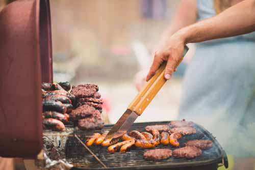 Man Cooking Burgers And Sausages On BBQ