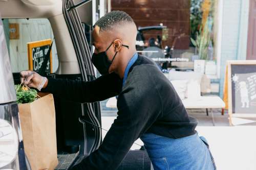 A Man Places Customer Order In Back Of Car Photo