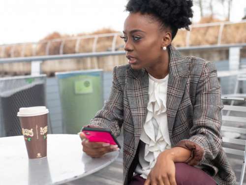 Young well dressed woman in tweed blazer holding smartphone - looking aw