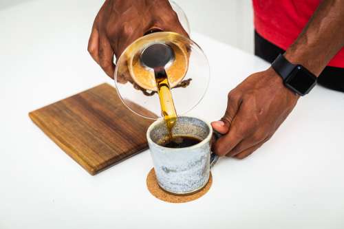 Man Holds Cup And Pours Black Coffee Photo