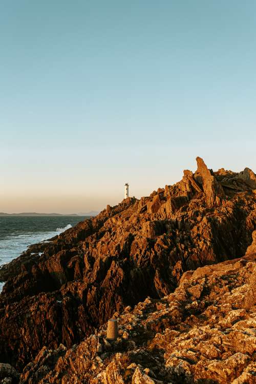 Tiny Lighthouse Beyond Rocky Shore Photo