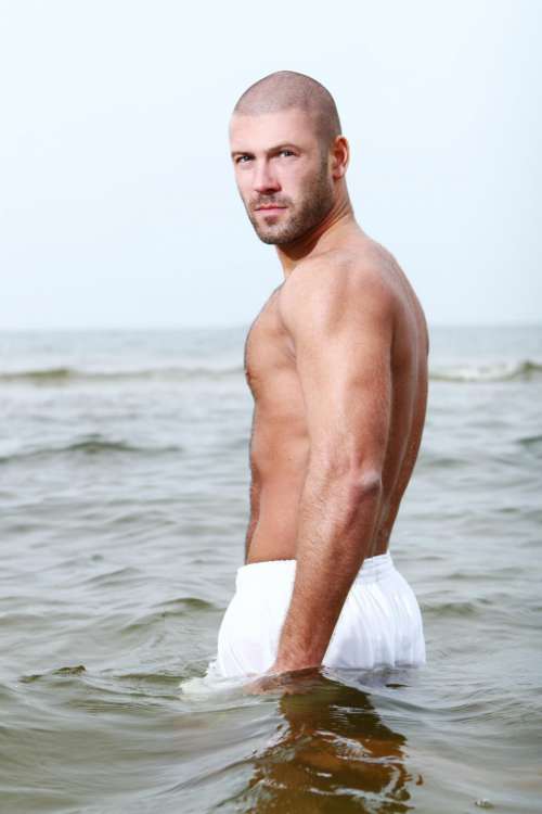 attractive man on beach, wading in deep water