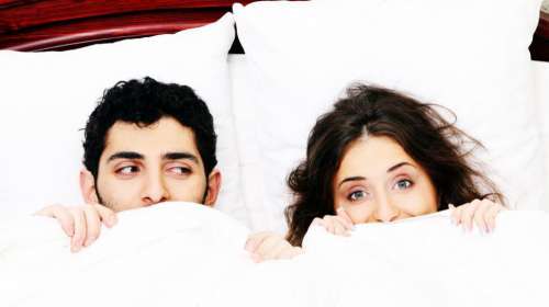 Young couple in bed with covers pulled up