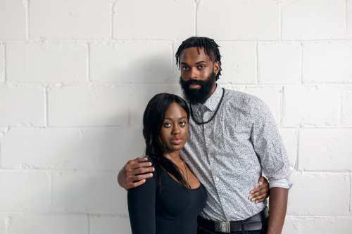 Couple Stand Against White Wall Looking At Camera Photo
