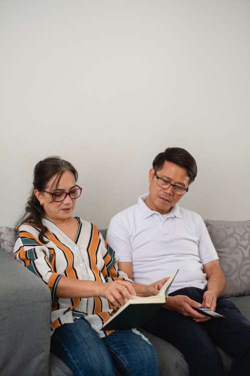 Woman Reading A Book While Man Looks Over Photo