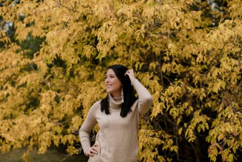 Woman In Tan Sweater Smiles Standing Against Yellow Trees Photo