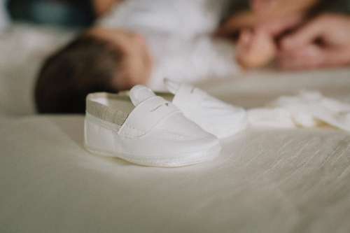Tiny White Baby Shoes On White Sheet Photo
