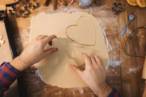 Man bakes cookies. Symbol of heart in dough on a wooden table in the kitchen