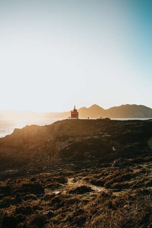 Lighthouse Peaks Over A Cliff At Sunset Photo