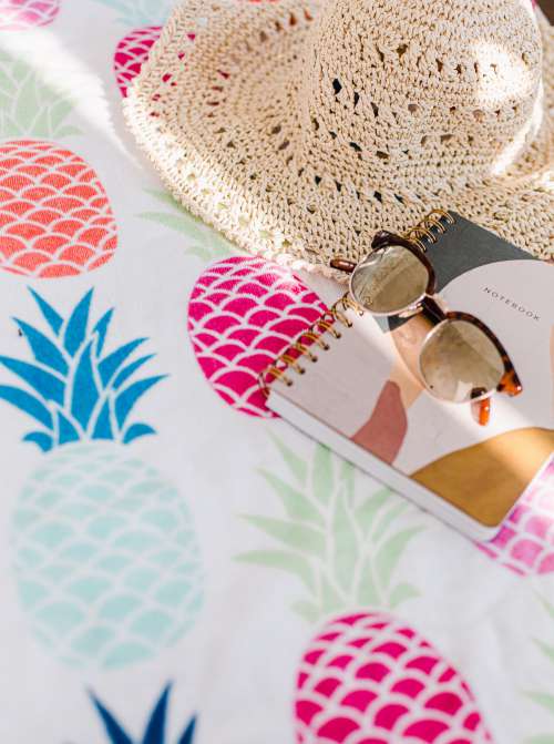 Notebook Sunhat And Sunglasses On Pineapple Table Cloth Photo