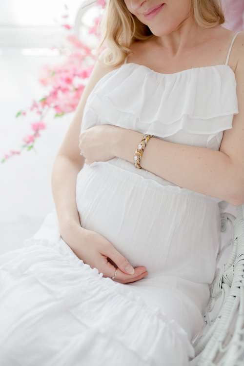 Woman In Soft White Dress Sits And Holds Her Pregnant Belly Photo