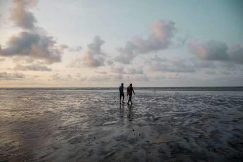 Two People Walking Along The Beach At Sunset Photo