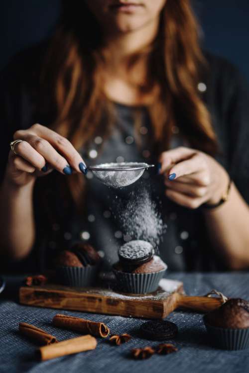 Woman dusting muffins with a powdered sugar