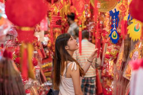 Person In A Market Is Surrounded By Red And Gold Items Photo