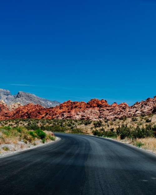Paved Road Bends With Red Rocky Hills In The Background Photo