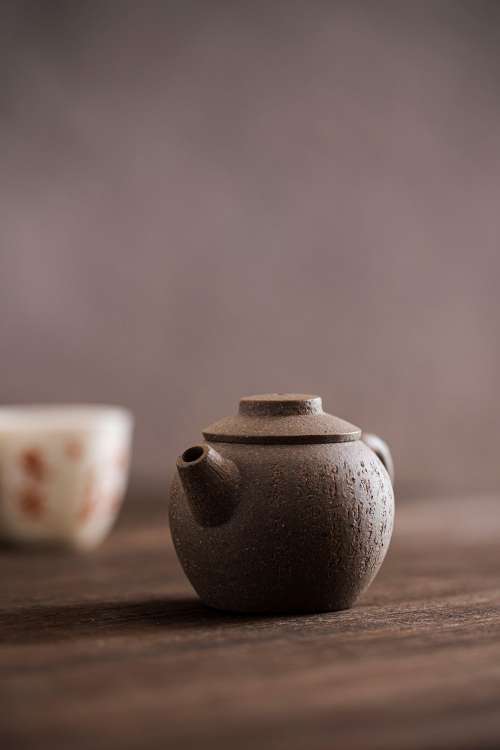 Small Brown Teapot With A White And Orange Cup Behind It Photo