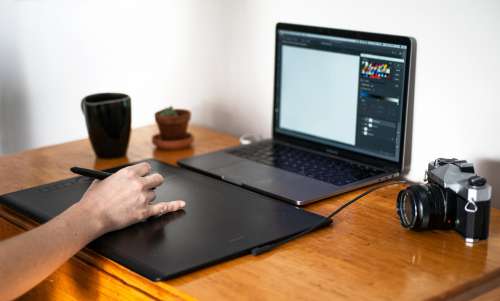 Hand Uses A Pen On A Large Tablet In Front Of A Laptop Photo