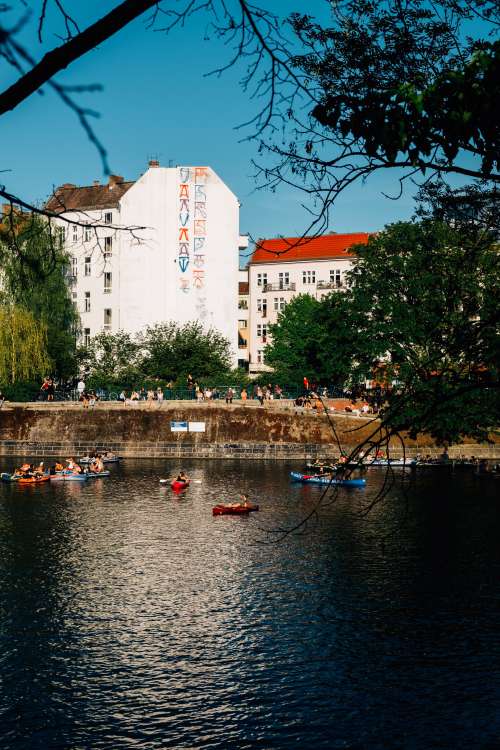 Kayaks Float In River With Buildings Behind It Photo