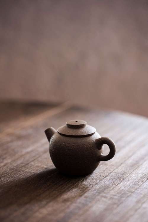 A Mini Brown Teapot With Carved Characters On A Wooden Tabletop Photo