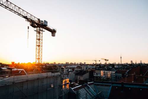 The Sunsets Over A City Rooftops And Tall Cranes Photo