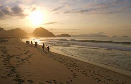 People Walking Down A Sandy Beach At Sunset Photo