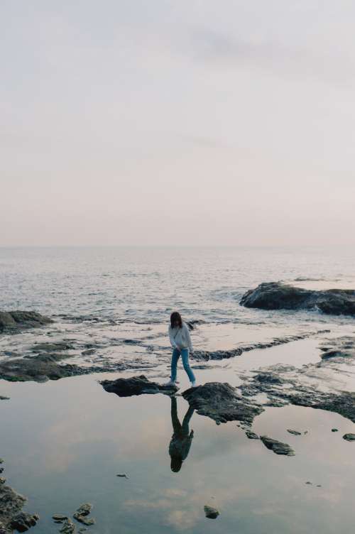 Person Stands On Rocks Poking Out Of The Ocean Shoreline Photo