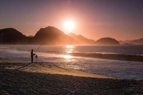 Person Fishing On The Beach Is Silhouetted At Sunset Photo