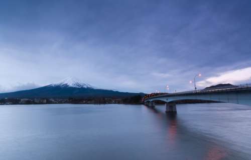 Bridge Over Still Water Reaches To A Large Snowy Mountain Photo